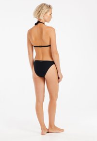 Czarny zestaw bikini z halterem, wykonany z teksturowanej tkaniny, z dopasowanymi majtkami. Prosty design bez widocznych logo i wzorów.