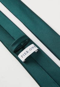 Corbata de satén en color verde azulado con una textura suave. Presenta un lazo para ajuste y una etiqueta blanca con "PIER ONE" en letras serif azules.