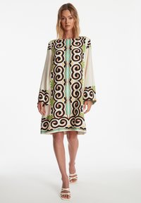 Patronen jurk met lange mouwen, met gedurfde zwarte, groene en oranje ontwerpen op een crème achtergrond. Glad, lichtgewicht stof.