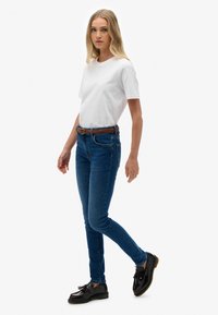 Camisa blanca de manga corta, jeans skinny azules con diseño de cinco bolsillos, cinturón tejido marrón, zapatos negros de cordones con borlas.