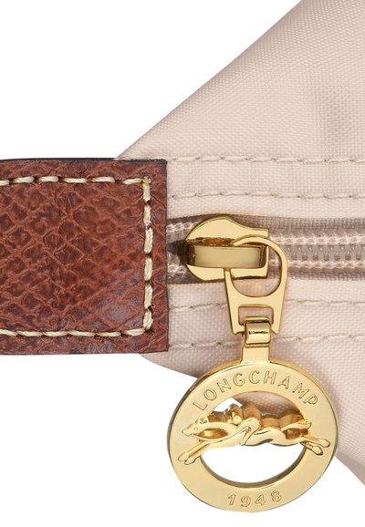 Beige fabric pouch with brown textured leather trim, gold zipper, and circular gold logo tag featuring a running horse, labeled "LONGCHAMP 1948."