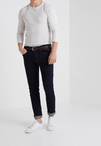 Ljusgrå långärmad topp kombinerad med mörkblå jeans, ett flätat brunt bälte och vita sneakers. Avslappnad passform med uppvikta ärmslut.
