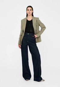 Roheline struktureeritud bleiser, must voodriga topp, tumedast denimist kõrge vöökohaga laiade säärtega püksid silmatorkavate õmblustega ja hõbedased aksentidega kingad.