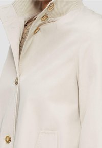 Beige jas met een geribbelde kraag, voorzien van gouden knopen, een zijzak en een gladde textuur, ontworpen voor een getailleerde silhouet.