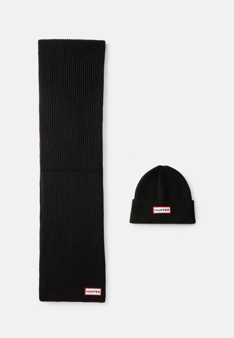 Fekete kötött sál és sapka szett, bordás textúrával. Mindkét darabon található egy fehér címke piros és fehér díszítéssel, amelyen az "HUNTER" felirat áll.