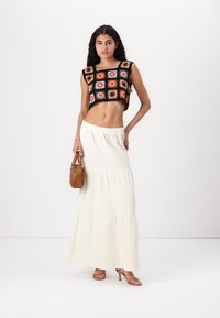 Kukičasti crop top s šarenim cvjetnim uzorcima; bijela višeslojna maksi suknja; smeškana torba; sandale s remenčićima u bež boji; glatka, lagana tkanina.