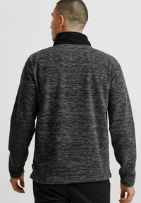 Donkergrijze fleece pullover met een hoge kraag, een textuurpatroon en lange mouwen. De zoom heeft een lichte boog en er zit een klein label aan de zijkant.