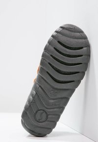 Black rubber shoe sole with pronounced treads and grooves, featuring a smooth texture and a circular logo. Edge is slightly raised, showing wear.