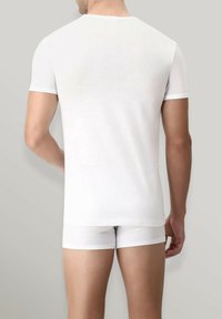 T-shirt bianca a maniche corte con collo rotondo, abbinata a slip bianchi. Texture liscia e design aderente. Sfondo neutro.