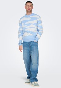 Blå strikketrøje med hvide skymønstre, parret med lyseblå posede jeans og grå sneakers, med ribbede manchetter og kant.