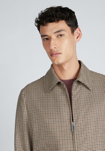 Brązowa i beżowa kurtka z zamkiem błyskawicznym w kratę, z wyrazistym kołnierzem, o gładkiej fakturze i metalowym wykończeniu zamka.