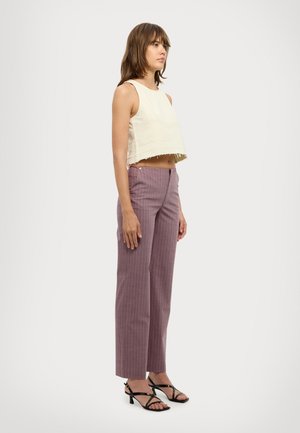 Top corto crema con orlo a frange, abbinato a pantaloni a righe verticali rosa e décolleté nere con cinturini. Silhouette slim fit.