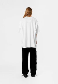 Camiseta blanca de gran tamaño con un detalle de parche en la parte trasera, combinada con pantalones negros holgados que presentan un acento gráfico en el costado.