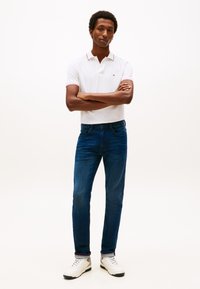 Polo bianca a maniche corte con dettagli rossi, abbinata a jeans blu scuro e sneakers bianche. Design semplice, forma aderente, tessuto morbido.