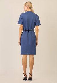 Abito blu a maniche corte, con cintura in vita di una fascia nera. Presenta un taglio dritto e un orlo che arriva fino al ginocchio.