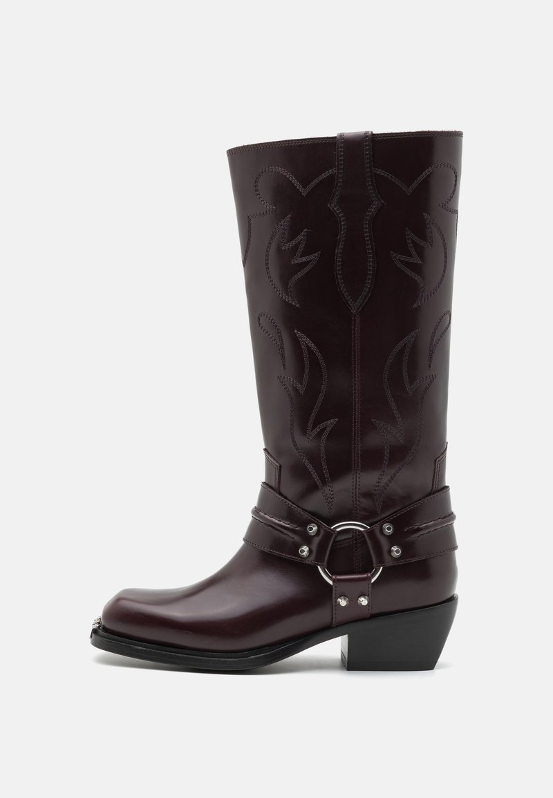 Botas de vaquero de cuero burdeos con costuras decorativas, punta curvada, una correa con hebilla de plata y un tacón bajo y grueso.