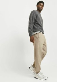 Grå tekstureret sweater lagd over en hvid skjorte, parret med beige tapered bukser og sølvfarvede sportssko, sat mod en ensfarvet baggrund.