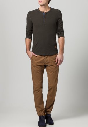 Donkergroen henley-shirt met lange mouwen en drie knopen, gecombineerd met beige chinos en marineblauwe schoenen. Simpele, casual pasvorm.