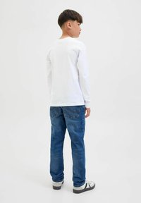 Maglietta bianca a maniche lunghe abbinata a jeans in denim blu e sneakers grigie con dettagli neri, vista da dietro.