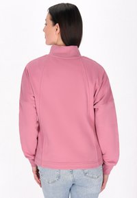 Fleecejack in zacht roze met een hoge kraag, raglanmouwen en rib gebreide manchetten. Gladde textuur met minimaal zichtbare stikseldetails.