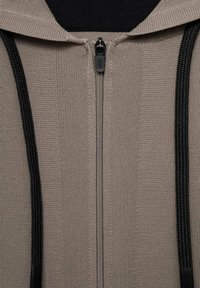 Beige rits-hoodie met zwarte trekkoorden, uitgevoerd in een gemêleerde brei-fabric en met een ritssluiting. Minimalistisch ontwerp zonder patronen.