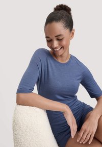 Blauwe, getailleerde, kortom shirt met een ronde halslijn en een zachte textuur, gedragen zittend op een lichte, gestructureerde ondergrond.