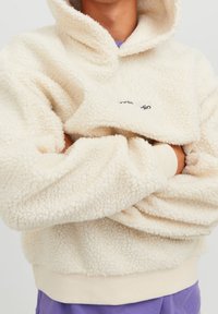 Felpa con cappuccio color crema in tessuto pile morbido e strutturato, con tasca a marsupio e vita aderente. Dettaglio logo nero sul petto.