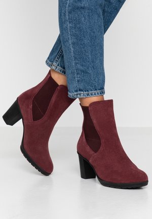 Ankelhøje bordeaux ruskind hælede støvler båret med opsmøgede blå jeans, der viser side elastiske paneler og sorte blokhæle.