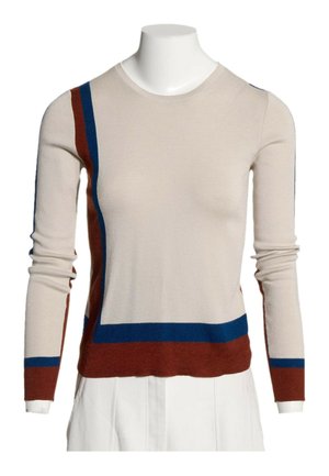 Pull beige à manches longues avec des rayures blocs bleu et rouille sur le côté gauche, les poignets et l’ourlet, porté sur un torse de mannequin blanc.