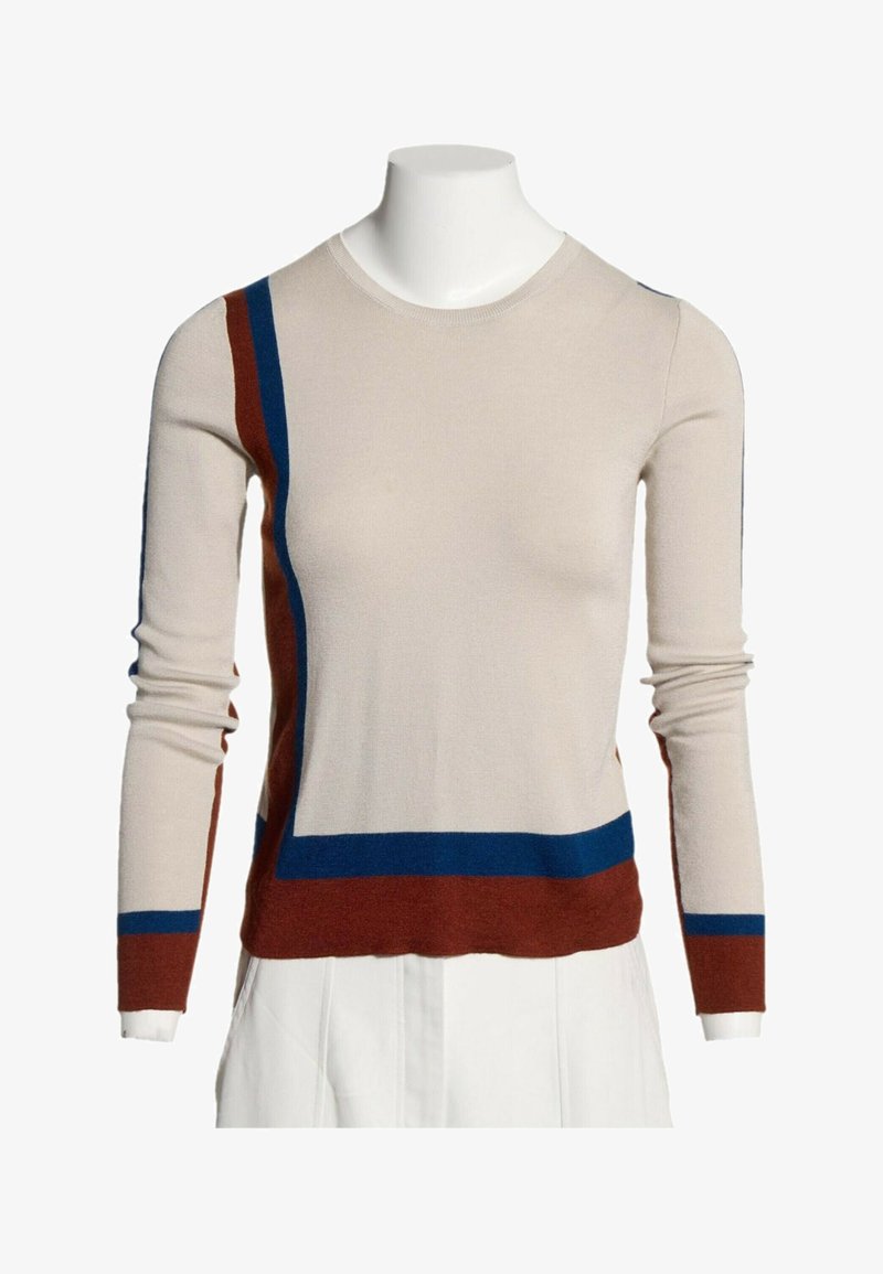 Pull beige à manches longues avec des rayures blocs bleu et rouille sur le côté gauche, les poignets et l’ourlet, porté sur un torse de mannequin blanc.