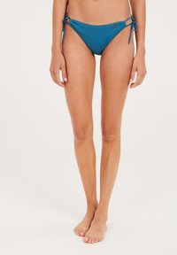 Tirkizni bikini don s bočnim vezanjem, s glatkom teksturom tkanine i minimalističkim oblikom, pogodan za plažni outfit.
