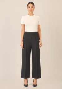 Pantalons plissés noirs taille haute avec jambes larges, associés à un haut ajusté blanc à manches courtes et des escarpins noirs à bout pointu.