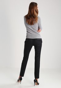 Grå stickad tröja med ribbad fåll som matchas med figurnära svarta byxor med bakfickor, och bärs med svarta högklackade skor.