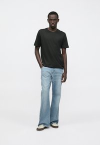 Černé tričko s kulatým výstřihem, světle modré rozšířené džíny a bílé tenisky. Hladká látka, volný střih a minimalistický design bez vzorů.