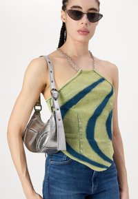 Green and blue patterned halter-top made from textured fabric, paired with a metallic silver handbag featuring a chain strap and zippers.