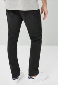 Musta farkut slim fit -mallilla, joissa on kaksi takataskua ja sileä, matta pinta. Yhdistetty valkoisiin lenkkareihin.