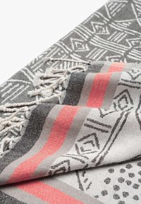 Tekstil dengan pola geometris hitam dan putih, menampilkan garis koral dan abu-abu. Dihiasi dengan sulaman di satu tepi.