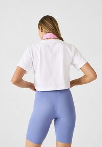 Witte cropped t-shirt met korte mouwen, gecombineerd met lichtblauwe fietsbroeken met textuur. De nek van het model is versierd met een roze sjaal met stippenpatroon.