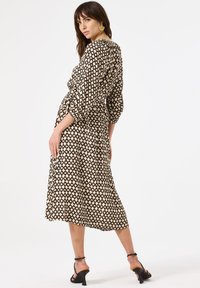 Midi-jurk in een crèmekleurig en zwart ruitpatroon, met 3/4 puffmouwen en een getailleerde taille, gecombineerd met zwarte hoge hakken.