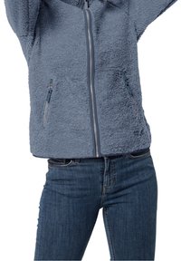 Kurtka z polaru w jasnoniebieskim kolorze z zamkiem błyskawicznym z przodu, dwoma bocznymi kieszeniami i teksturą przypominającą miękkie futro. Połączona z ciemnoniebieskimi dżinsami.