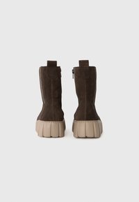Rudi suede batai su stores koncentruota bėgių, matomi iš nugaros ant šviesiai pilko fono.
