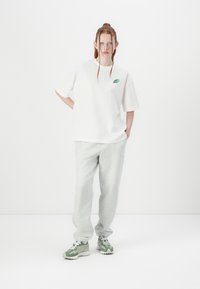 T-shirt en coton blanc surdimensionné avec un petit logo vert, associé à un pantalon de survêtement gris et des baskets avec des accents verts.
