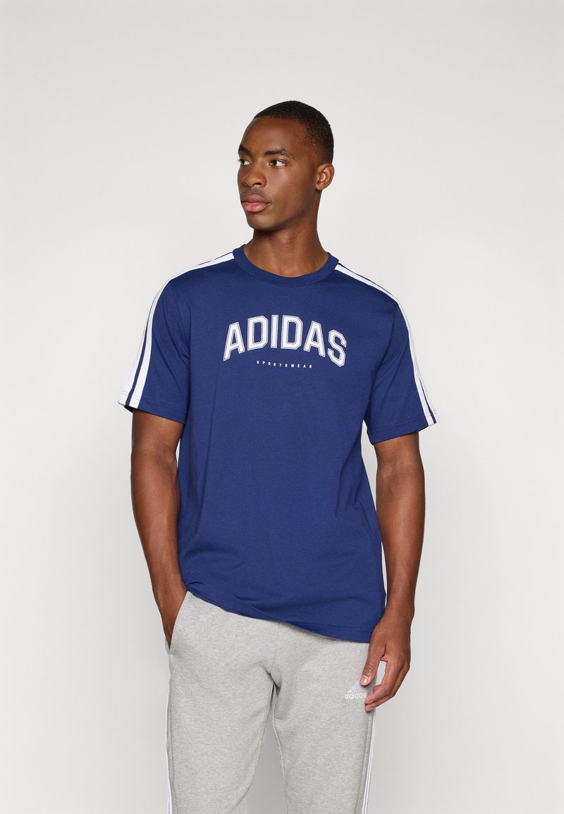 Granatowa koszulka z krótkim rękawem z białym logo "ADIDAS" oraz białymi paskami po bokach. Połączona z jasnoszarymi dresami.