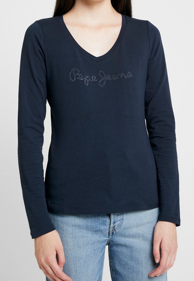 Marinblus med lång ärm och V-halsringning samt en texturerad "Pepe Jeans"-logotyp över bröstet. Tillverkad av mjuk bomull med en figursydd design.