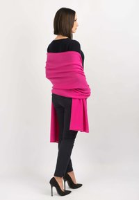 En varm pink sjal draperer over skuldrene og har en blød tekstur. Kombineret med sorte tætsiddende bukser og sorte stiletto hæle med naglede accenter.