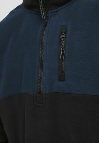 Fleece pullover with half-zip, featuring a dark blue top and black bottom. Includes a zippered pocket and a textured fabric.