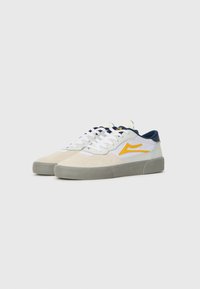 Baskets blanches et grises avec des accents bleus et un logo jaune. Comprennent des matériaux en daim et en maille avec une semelle en caoutchouc texturée.
