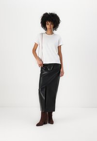 Hvid bomulds t-shirt kombineret med en sort faux læder midi nederdel med en forside split, suppleret med brune ruskinds ankelstøvler og en pink taske.