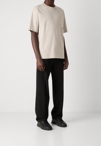 Beige kortärmad t-shirt i bomull med bröstficka, i kombination med svarta vida byxor och svarta sneakers. Enkel, minimalistisk design.