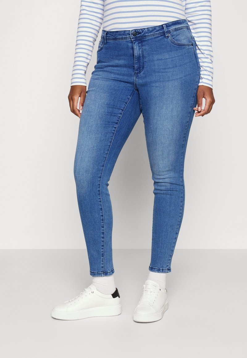 High-waisted blue denim jeans with a slim fit, featuring five-pocket design and subtle fading. Worn with white sneakers and socks.